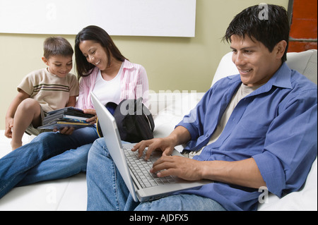 Father Using Laptop and mother and son Looking at DVDs on Couch Stock Photo