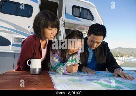 Two parents and daughter looking at map on picnic table outside RV Stock Photo