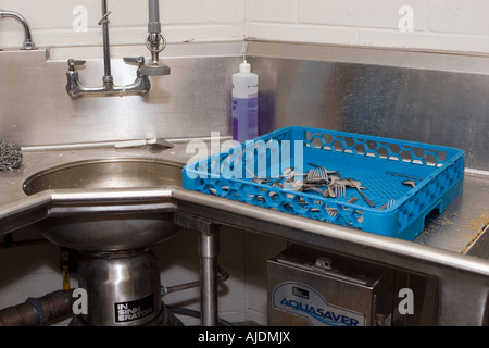 Dirty utensils rinsed in sink and passed on to dishwasher to be cleaned in school kitchen Stock Photo