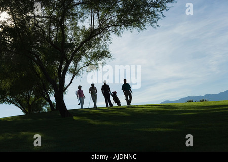 Silhouettes of group of golfers walking on golf course Stock Photo