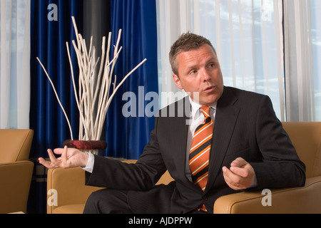 Businessman sitting in a chair talking looking slightly to the right of camera Stock Photo