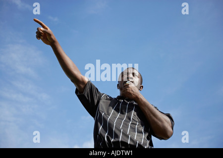 Soccer referee blowing whistle and pointing, portrait, low angle view Stock Photo