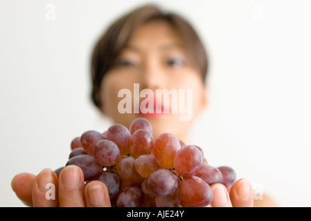 Attractive young Korean Asian woman holding bunch of grapes; focus on grapes Stock Photo