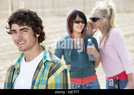 Young man smiling with women whispering behind Stock Photo