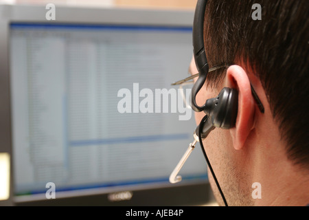 A male analyst working at a computer with a headset shot from behind focus on headset Stock Photo