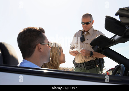 Police officer issuing ticket to couple in car Stock Photo