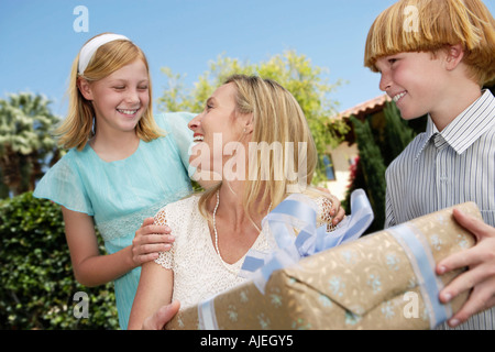 Smiling mother receiving gift from children outside Stock Photo
