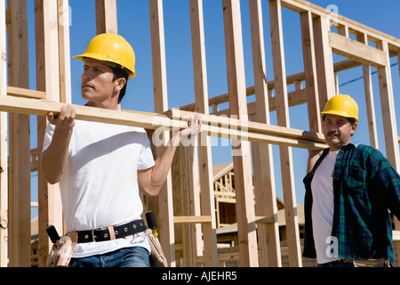 Two construction workers carrying lumber on construction site Stock Photo