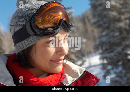 Young woman wearing ski goggles on head in snow, portrait. Stock Photo