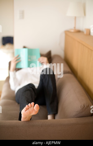 Young woman reading book lying on sofa Stock Photo