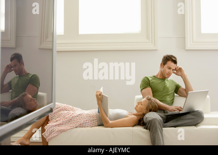 Couple relaxing together on sofa, man using laptop, woman reading Stock Photo
