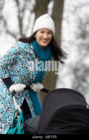 Mother walking with baby carriage in park, (portrait) Stock Photo