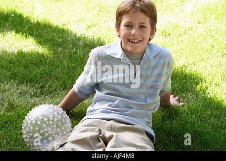 Boy with ball sitting on park lawn, portrait Stock Photo