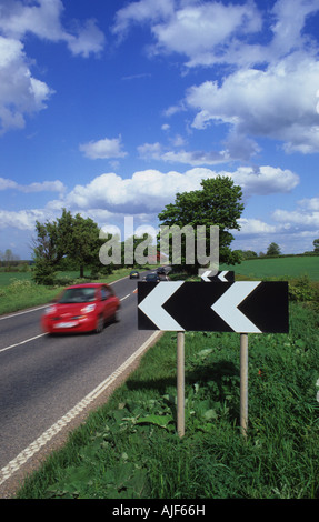 traffic passing black and white chevron warning signs of sharp bend on country road leeds yorkshire uk Stock Photo