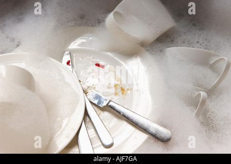 Stack of Dirty Dishes and silverware in Sink with bubbles, close-up Stock Photo