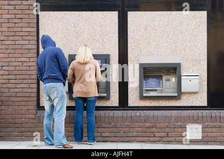 Thief looking over womans shoulder at cash machine Stock Photo