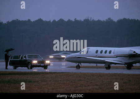 Chauffeur waiting by limousine for passengers on private plane disembarking in the rain Stock Photo
