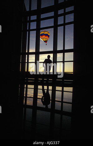 Silhouetted man looking at hot air balloon through big lobby windowWith thoughts of escaping Stock Photo