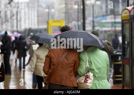 two female friends share an umbrella in the rain whilst walking along belfast city centre shopping area Stock Photo