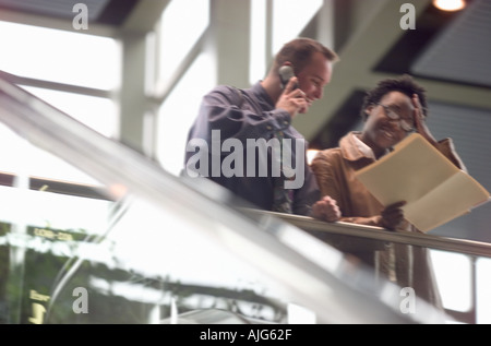Male and female executive reading report and using cell phone Stock Photo
