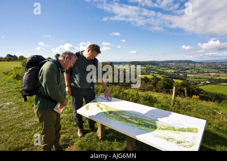 Two hikers on the Cotswold Way enjoying the view out over the Severn Vale from Coaley Peak Picnic Site, Gloucestershire Stock Photo