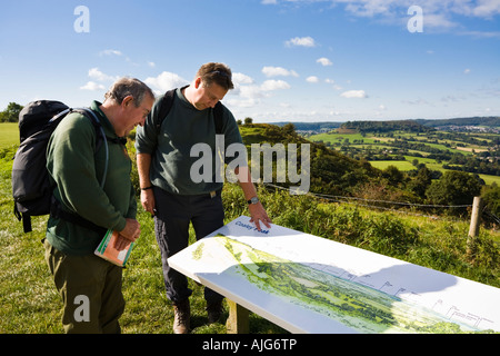 Two hikers on the Cotswold Way enjoying the view out over the Severn Vale from Coaley Peak Picnic Site Gloucestershire Stock Photo