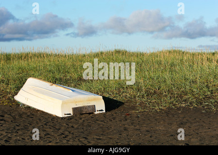 A single white boat lying upside down on the beach sand dunes and clear skies Stock Photo