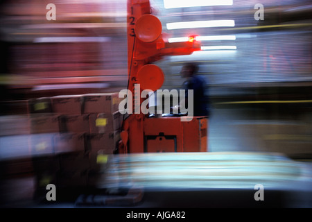 Motion blur image of an African-American workman driving a forklift through a warehouse Stock Photo