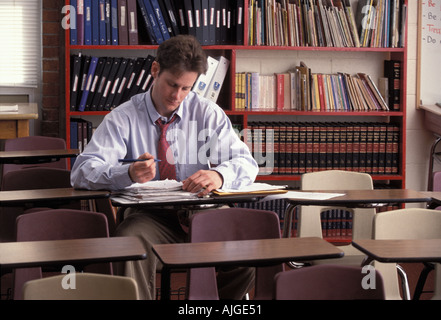 Caucasian male teacher working alone on students papers after hours in an empty classroom Stock Photo