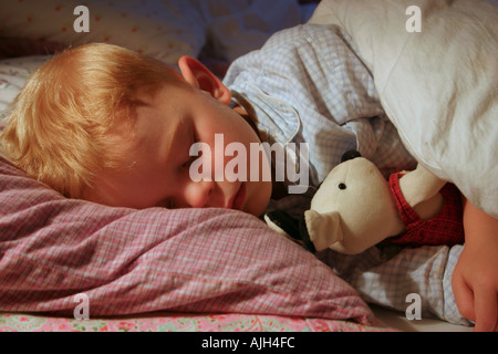 three year old boy asleep in bed with a soft toy Stock Photo