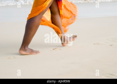 Colour landscape of woman walking along beach in sarong. Stock Photo