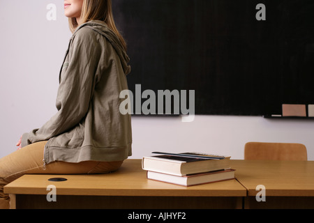 Young woman sitting on edge of desk Stock Photo