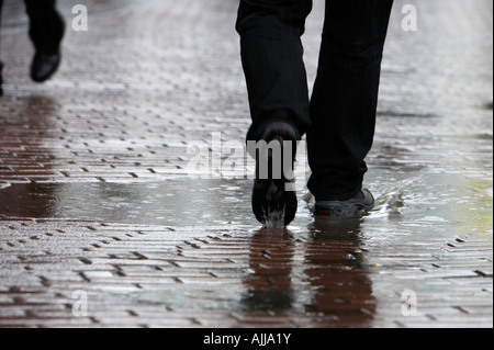 man walking through puddle of water pool in pedestrian area of belfast city centre Stock Photo