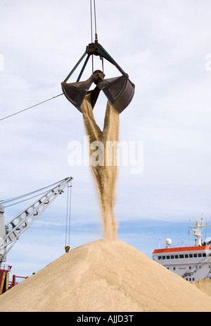 A clamshell bucketloader is seen dumping sand against a blue sky with light clouds. Stock Photo