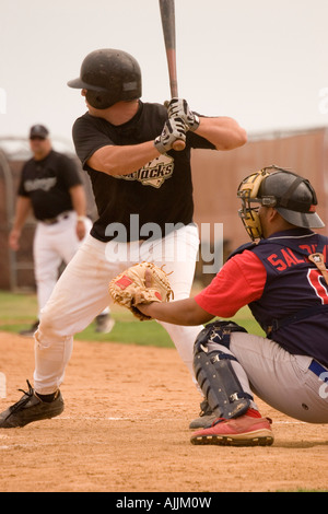 Photo of a batter, a catcher, and a base coach during a baseball game.  The batter is waiting for the pitcher to throw the ball. Stock Photo