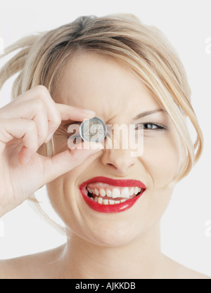 Woman holding Euro coin to her eye Stock Photo