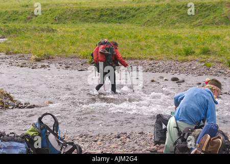 A couple crossing a river on Umnak Island in the Aleutian Islands Alaska Stock Photo