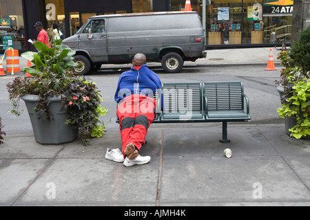 A tired young man takes a nap on a public bench in midtown Manhattan Stock Photo