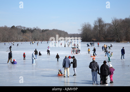 Dozens of people spread out across the lake skating sledding, playing hockey and  small children being dragged on sledgesg Stock Photo