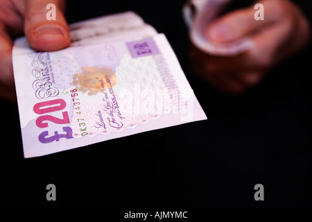A man hands over a twenty british pound note from a bundle of cash Close crop of hands against black background Stock Photo