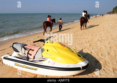 Tourists ride on horseback past a jet ski on the beach at Batu Ferringhi, Penang Island, Malaysia. Stock Photo