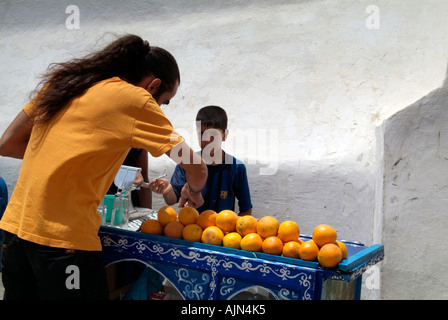 A young man serving a Moroccan boy freshly squeezed orange juice from his blue cart piled with fresh oranges in the Medina. Stock Photo