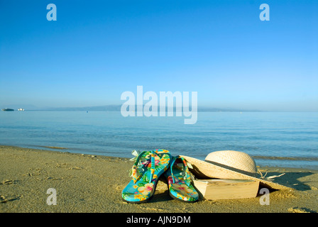 Holiday props book star sun hat on waters edge sandy Mediterranean beach blue sea and sky in background Stock Photo