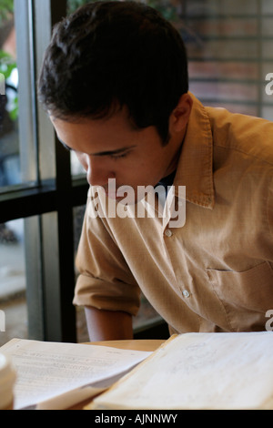 Young man studying by window He is looking over some papers he has on a table Stock Photo