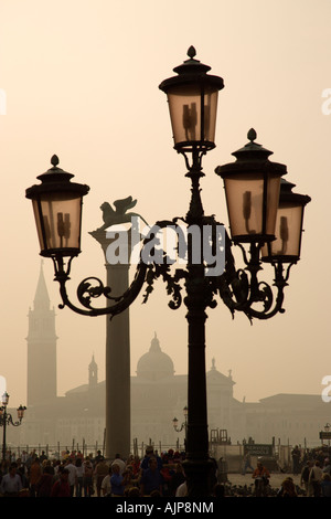 ITALY Veneto Venice Tourist crowd in Piazzetta under ornate lamppost with Palladio's San Giorgio Maggiore in mist of the lagoon Stock Photo