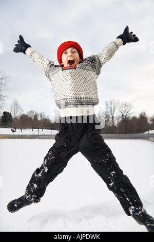 Excited Caucasian boy wearing sweater and red winter cap jumping in air with arms and legs outstretched Stock Photo