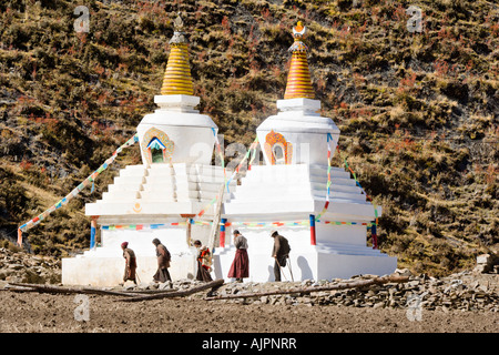 One legged man on crutches following Tibetan folks circumambulating chortens (Tibetan stupas), Daocheng, Sichuan, China Stock Photo