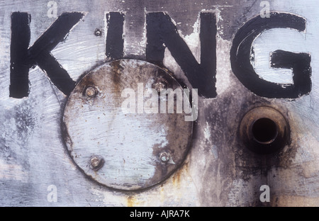 Close up of weathered scratched and stained white paint on boat hull with bolted metal disc bilge pump hole and word KING Stock Photo