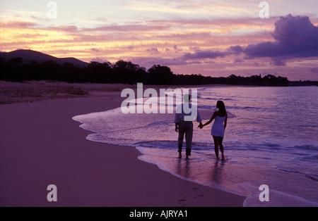 A romantic view of a young couple walking at the water's edge at sunrise at Makena, Maui. Stock Photo
