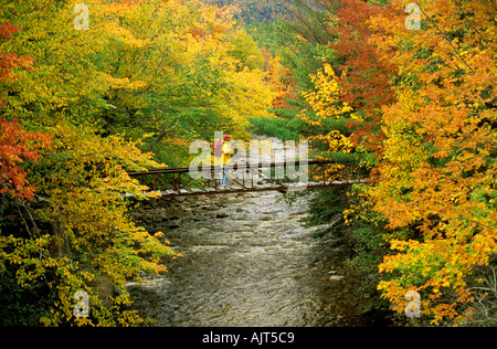 CANADA Nova Scotia Cabot Trail Woman hiker crossing Little River foot bridge surrounded by a spectrum of autumn colors Stock Photo
